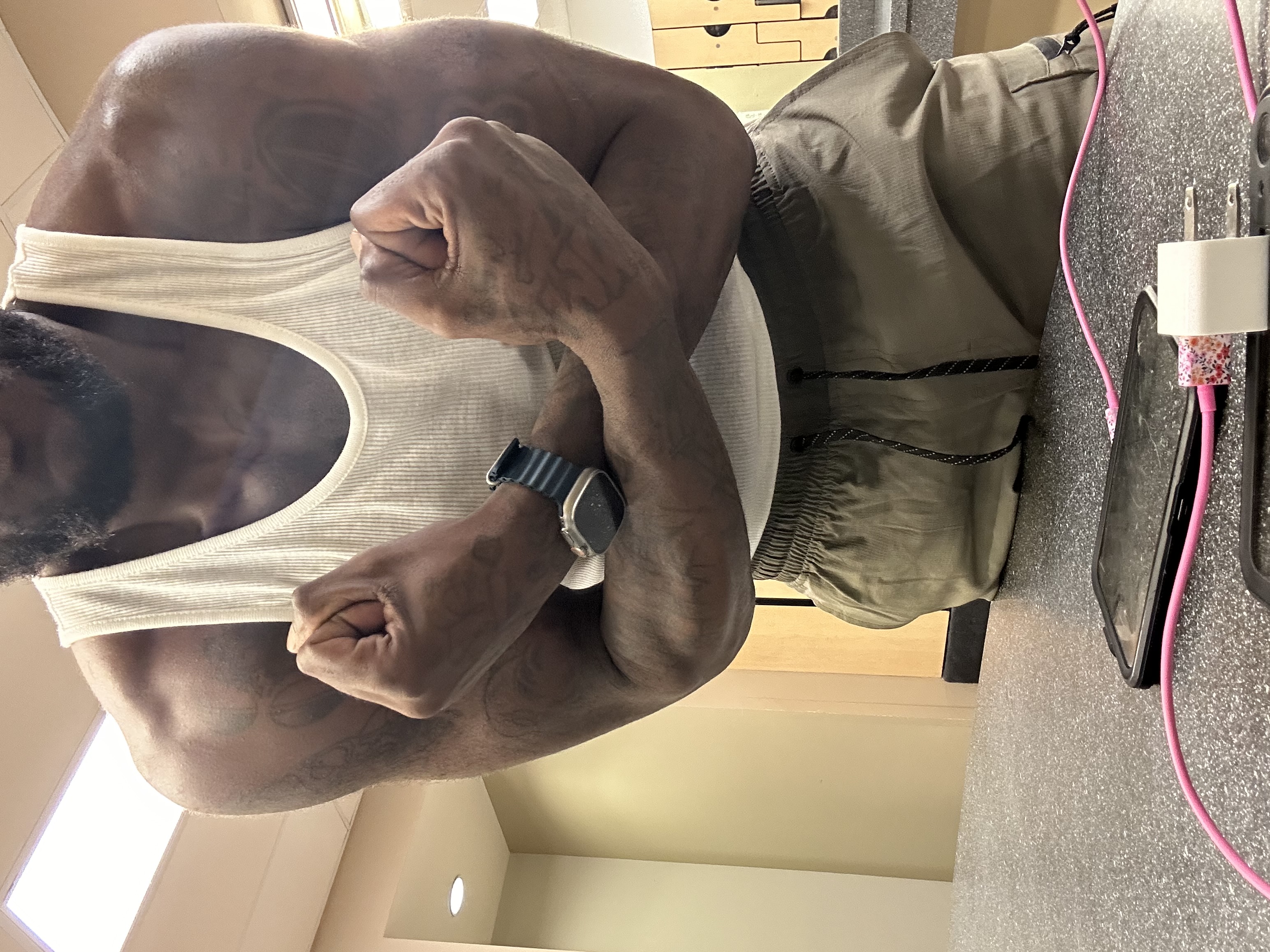 Sahun Rattary flexing in a white tank top at home